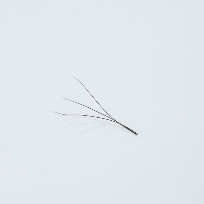 Κοντινή λήψη (macro) ενός έτοιμου fanβλεφαρίδων (premade fan) 3D, αποτελούμενου από 3 λεπτές, μαύρες ίνες ενωμένες στη βάση με μακρύ κορμό (long stem), για τεχνική volume με φυσικό αποτέλεσμα.