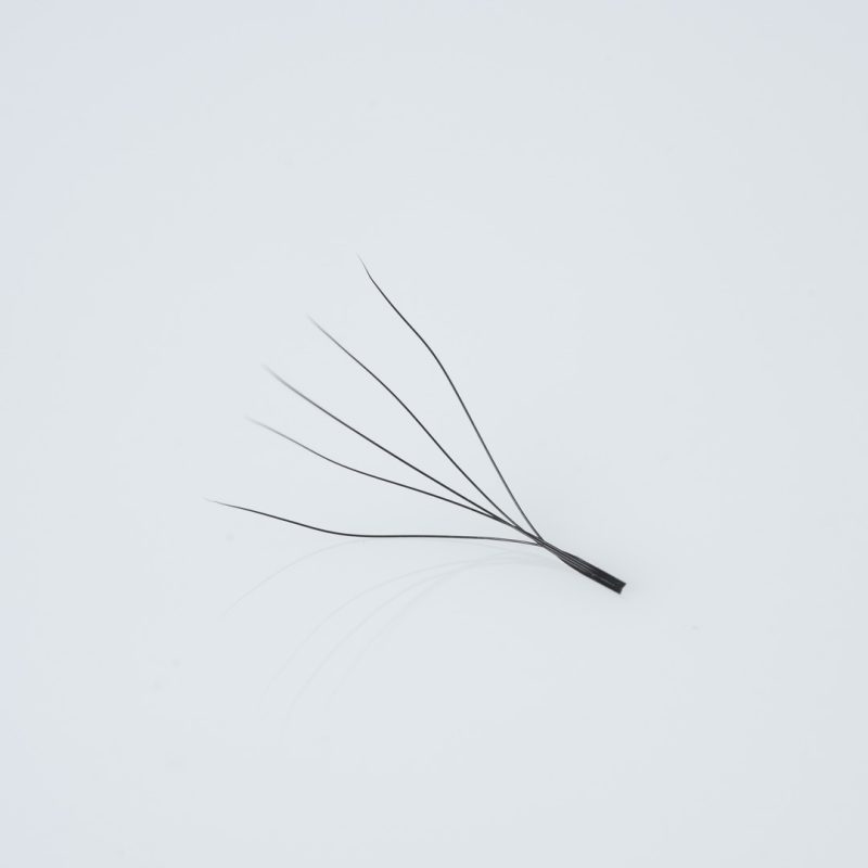 Κοντινή λήψη (macro) ενός έτοιμου pre made fan βλεφαρίδων (premade fan) 5D, αποτελούμενου από 5 λεπτές, μαύρες ίνες ενωμένες στη βάση με μακρύ κορμό (long stem), κατάλληλο για τεχνική volume extensions.